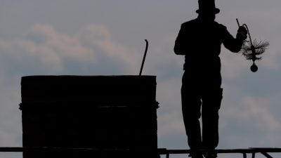 Ein Schornsteinfeger mit seinem Kaminkehrerwerkzeug auf einem Dach.