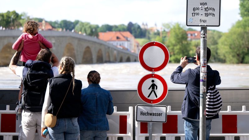 Menschen schauen sich in der Altstadt am Donauufer hinter einer Schutzwand das Hochwasser an.