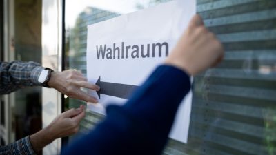 Wahlhelfer hängen einen Zettel, auf dem „Wahlraum“ steht, auf.