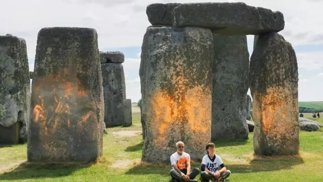 Demonstranten von «Just Stop Oil» sitzen vor dem Steinmonument Stonehenge, das sie zuvor mit orangener Farbe besprüht haben.