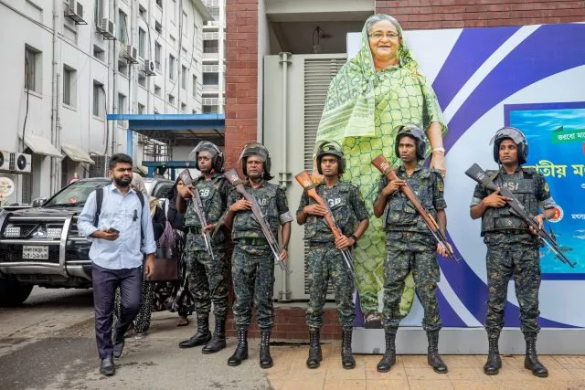 Militärangehörige stehen vor einem großen Porträt von Premierministerin Sheikh Hasina. Sie gilt als autokratisch regierende Premierministerin.