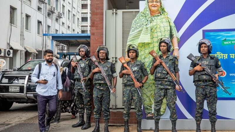 Militärangehörige stehen vor einem großen Porträt von Premierministerin Sheikh Hasina. Sie gilt als autokratisch regierende Premierministerin.