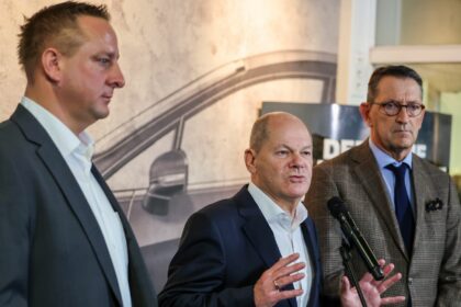 Betriebsratschef Benjamin Gruschka (l) neben Bundeskanzler Olaf Scholz (SPD) und Marcus Wassenberg (r), Geschäftsführer der Ford-Werke.