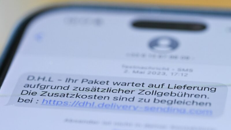 Auf einem Smartphone ist eine Betrugs-SMS zu lesen, in der Kriminelle ein Paket ankündigen und dafür Zollgebühren einfordern.