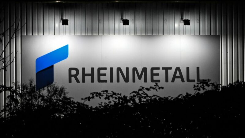 Das beleuchtete Logo und der Schriftzug der Rüstungsfirma Rheinmetall hängt an einer Produktionshalle.