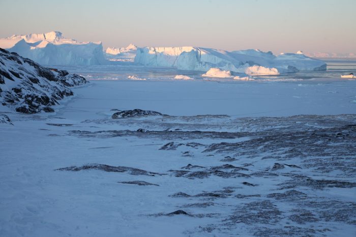 Eisberge ragen im Ilulissat-Eisfjord hinter einer verschneiten Gesteinslandschaft in die Höhe.