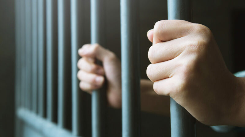 Man in prison hands of behind hold Steel cage jail bars. offender criminal locked in jail. Foto: Rattankun Thongbun/iStock