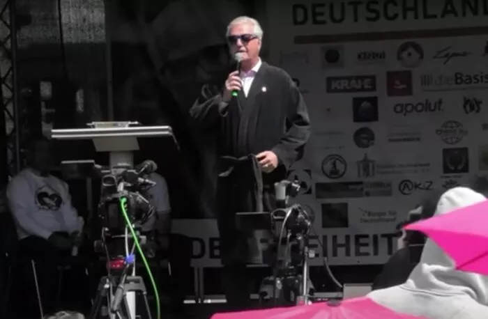 Am Samstag, 24. Mai 2025, trat der „COMPACT“-Herausgeber Jürgen Elsässer im Bademantel auf der Bühne einer Friedensdemonstration am Brandenburger Tor in Berlin auf – in erinnerung an eine frühmorgendliche Hausdurchsuchung vom Sommer 2024. Foto: Bildschirmfoto/Politik spezial