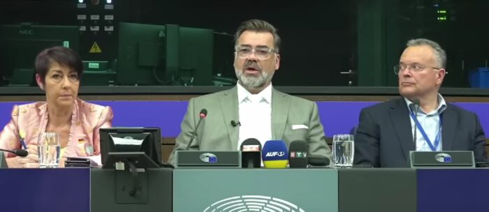 Der Datenanalyst Tom Lausen (Mitte) schilderte seine Sicht auf die Coronajahre am 7. Mai 2025 vor dem EU-Parlament. Er wird flankiert von den EU-Abgeordneten Christine Anderson (AfD) und Gerald Hauser (FPÖ). Foto: Bildschirmfoto/YouTube/Report24