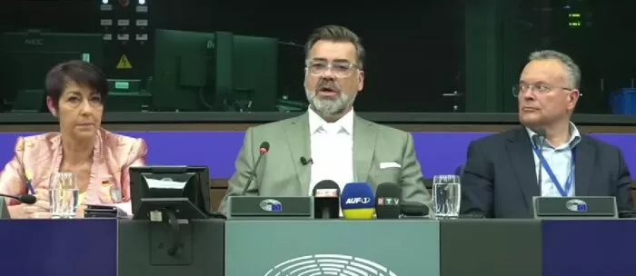 Der Datenanalyst Tom Lausen (Mitte) schilderte seine Sicht auf die Coronajahre am 7. Mai 2025 vor dem EU-Parlament. Er wird flankiert von den EU-Abgeordneten Christine Anderson (AfD) und Gerald Hauser (FPÖ). Foto: Bildschirmfoto/YouTube/Report24