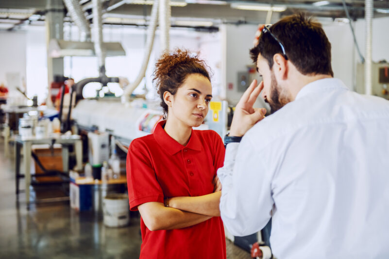 Serious cute caucasian female employee standing with arms crossed and listening angry director. Printing shop interior. iStock/dusanpetkovic