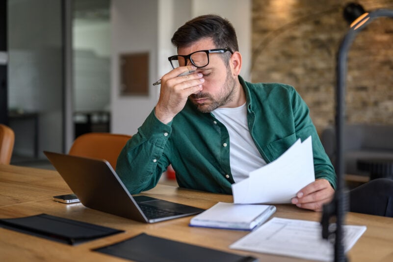 Anxious male financial advisor rubbing eyes while working over laptop and analyzing reports at desk Foto: Moon Safari/iStock