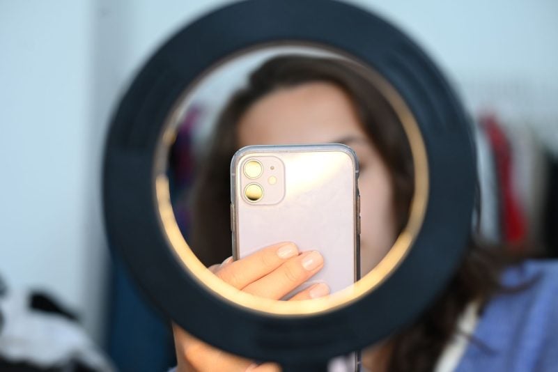 Eine Frau sitzt hinter einem Ringlicht und macht dabei Aufnahmen von sich (Symbolbild)