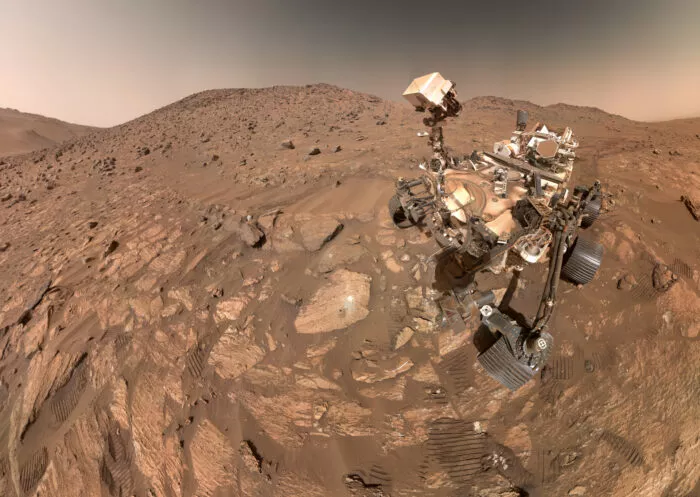 „Selfie“ des Mars-Rovers „Perseverance“ vom 23 Juli 2024 nach erfolgreicher Probenentnahme aus „Cheyava Falls“. Der kleine schwarze Punkt auf dem Stein links neben dem Rover ist jene Stelle der Kernbohrung, die weiße Fläche darüber der Ort weiterer Untersuchungen mit den Bordinstrumenten.