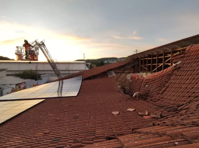 Vom Korb einer Drehleiter heraus kontrolliert ein Feuerwehrmann den eingestürzten Dachbereich.