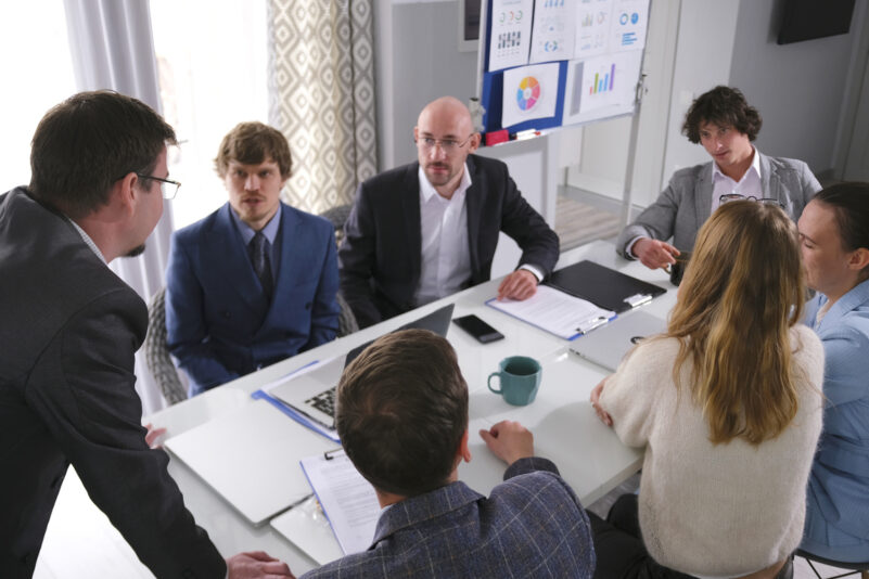 The concept of discussing the terms of cooperation and business development of the company. Young professionals are sitting at a table in a conference room. They are all dressed in business clothes and engaged in conversation. iStock/chekat