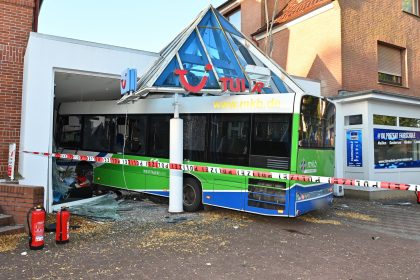 Bus kollidiert mit Auto und kracht in Reisebüro