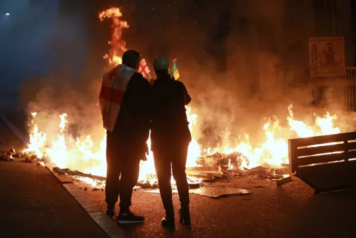 Demonstranten mit einer georgischen und einer ukrainischen Nationalflagge stehen im Stadtzentrum von Tiflis hinter einer brennenden Barrikade während einer Kundgebung der Opposition, bei der sie die Kommunalwahlen boykottieren und die Freilassung politischer Gegner fordern.