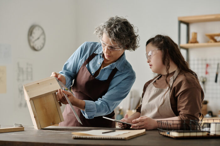 Girl with down syndrome and carpenter using ruler to measure house together while working in workshop